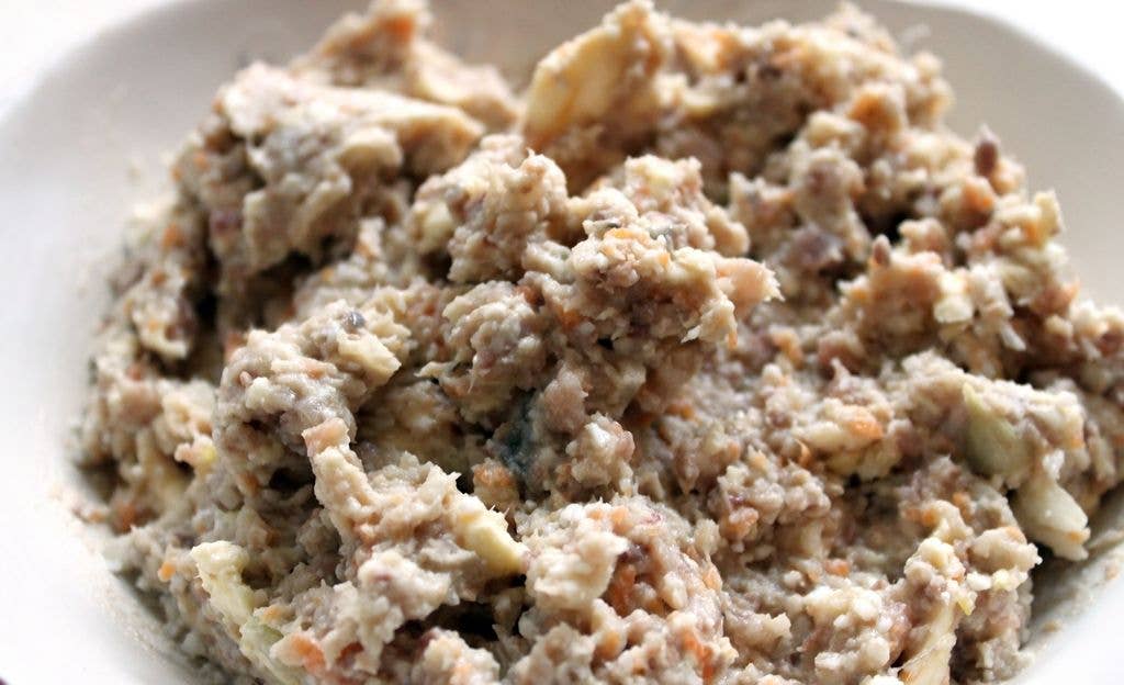 A white bowl filled with a coarse, textured mixture of minced herring and finely chopped vegetables, shown in close-up.