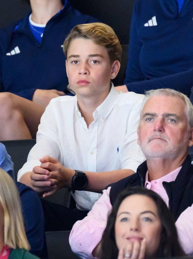 Prince George sits in stands with family, wearing white shirt